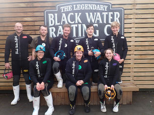 Leading Edge team posing in front of black water rafting sign